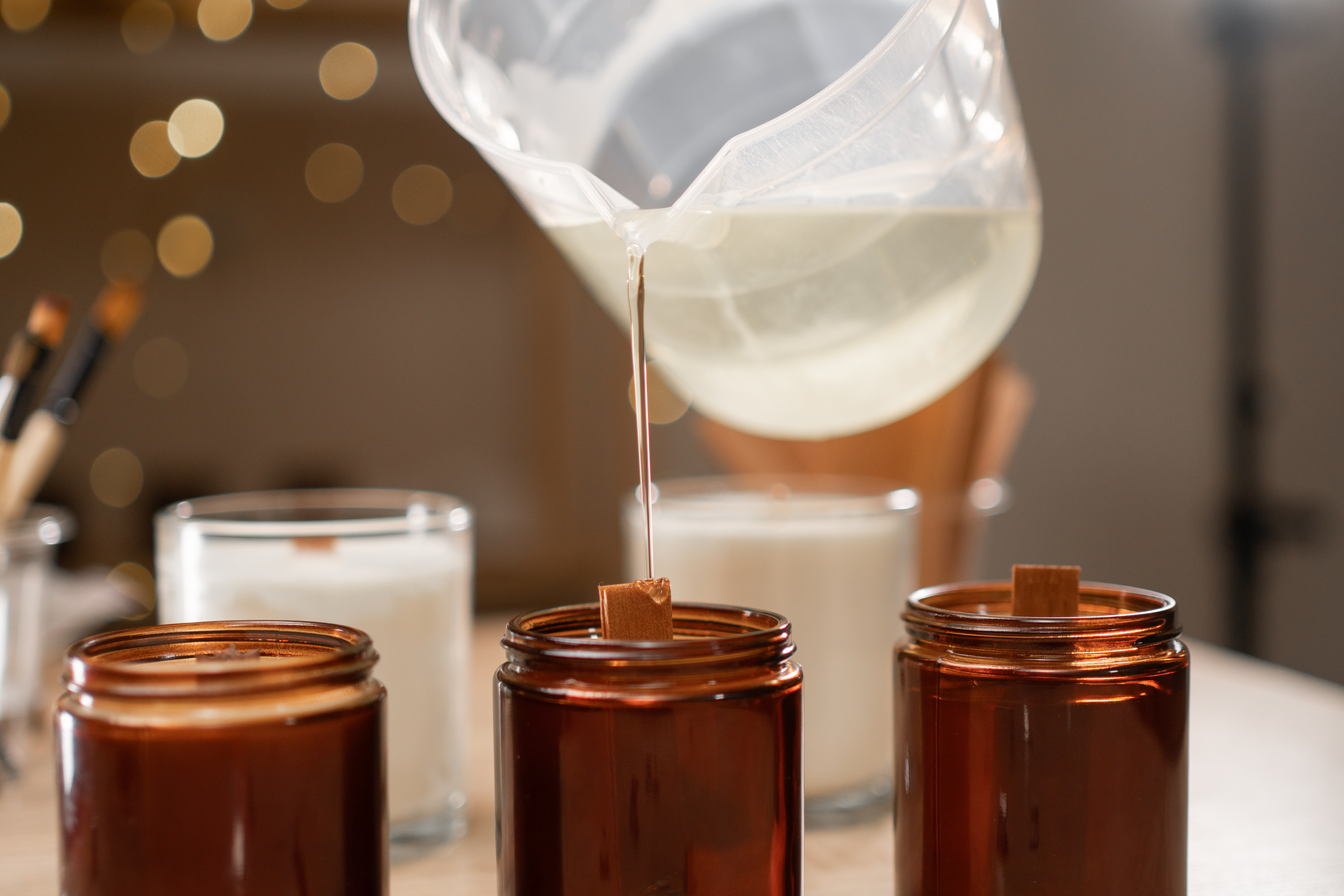 Concept of creative hobby and handmade candles. Close-up of female hands pouring melted soy wax into jar.